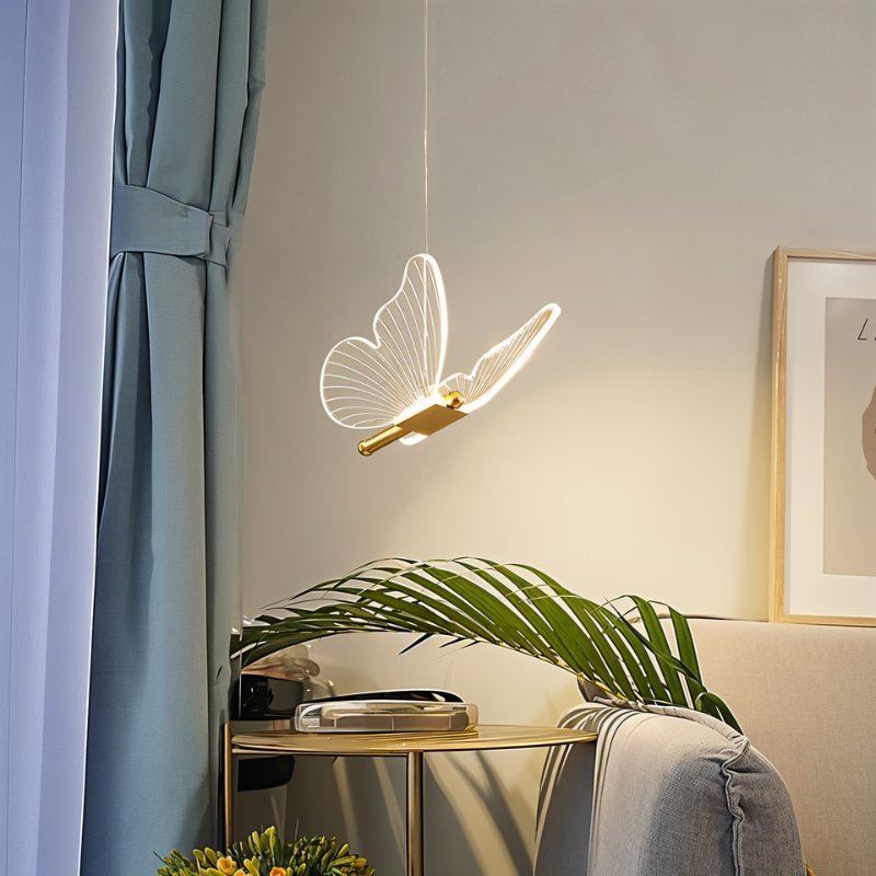 Clérachic brass butterfly pendant light glowing warm white above a round gold side table in a living room.