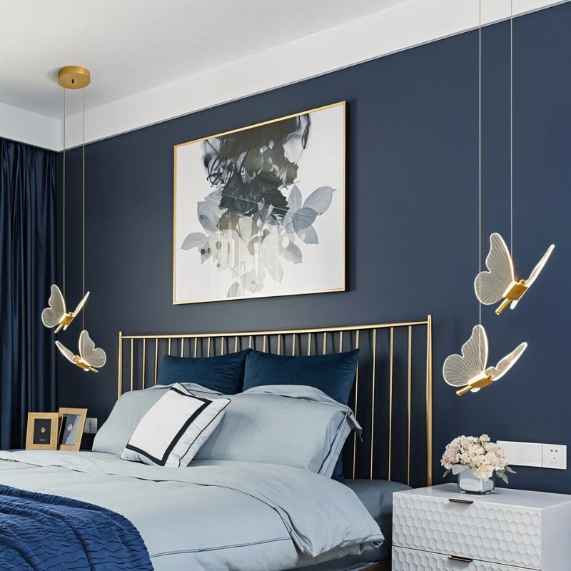 Clérachic brass butterfly pendant lights flanking a gold bed frame in a bedroom with a navy accent wall.