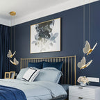 Clérachic brass butterfly pendant lights flanking a gold bed frame in a bedroom with a navy accent wall.