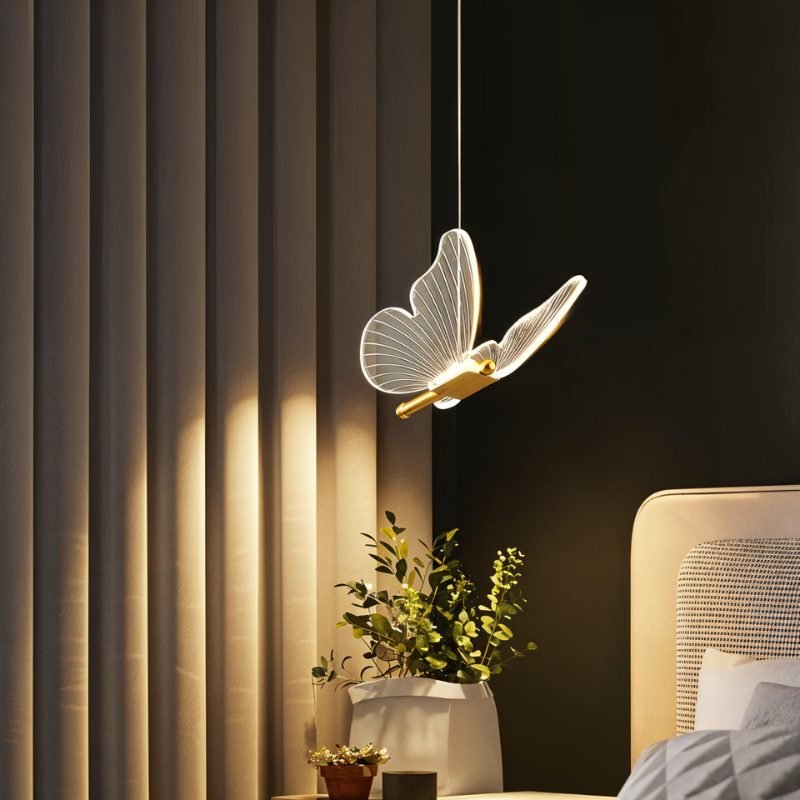 Clérachic brass butterfly pendant light glowing warm white beside a nightstand plant and pleated curtains.