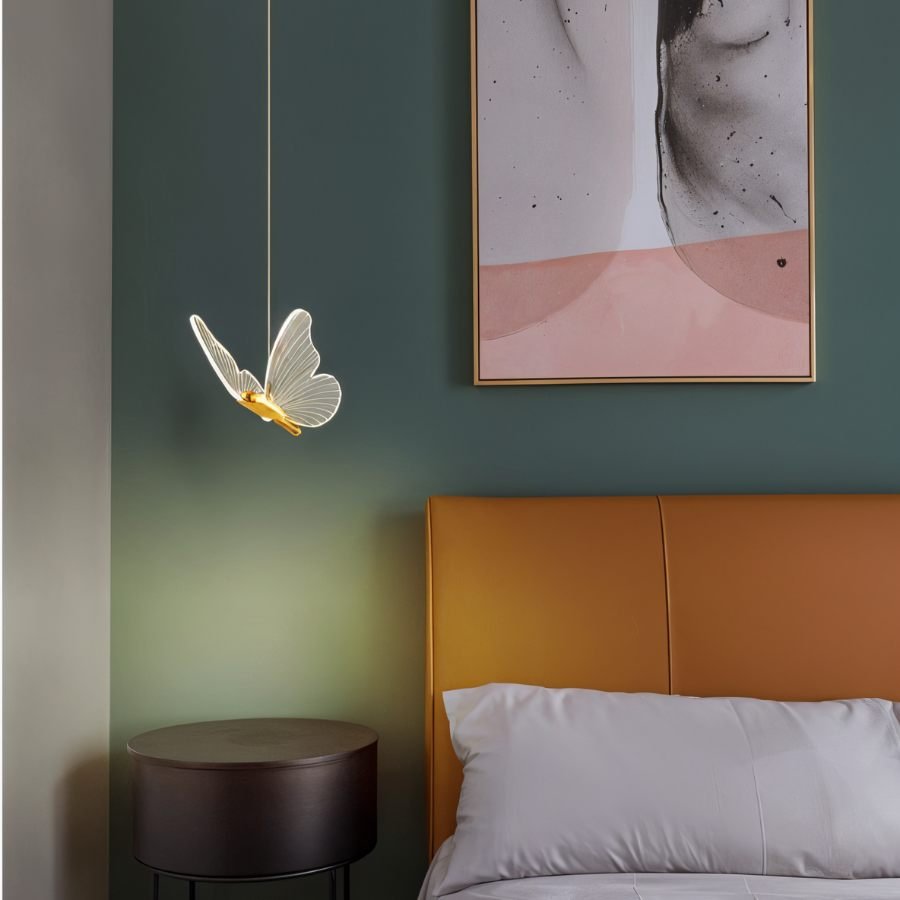 Clérachic brass butterfly pendant light glowing warm white beside an orange leather headboard and round nightstand.