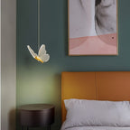 Clérachic brass butterfly pendant light glowing warm white beside an orange leather headboard and round nightstand.