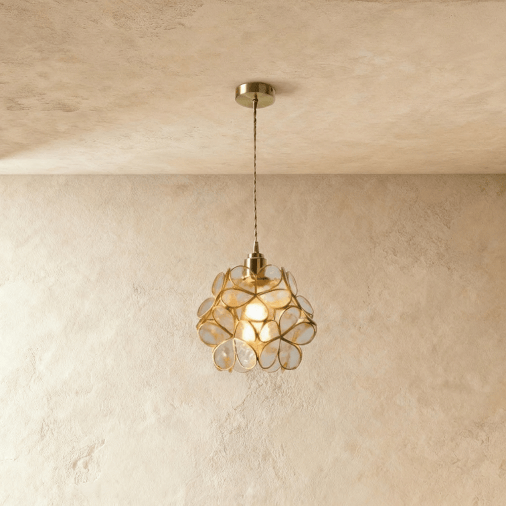 Clérachic single pendant with clear glass petals in brass wire, on a twisted cord from a brass ceiling plate, against limewash.