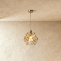Clérachic single pendant with clear glass petals in brass wire, on a twisted cord from a brass ceiling plate, against limewash.
