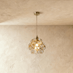 Clérachic single pendant with clear glass petals in brass wire, on a twisted cord from a brass ceiling plate, against limewash.