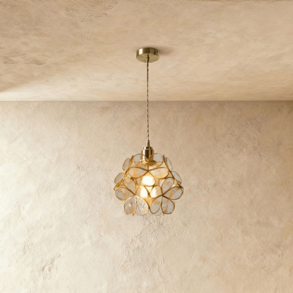 Clérachic single pendant with clear glass petals in brass wire, on a twisted cord from a brass ceiling plate, against limewash.