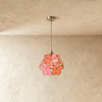 Clérachic single pendant of pink and coral glass petals edged in brass, hung on a twisted cord against limewash.