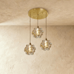 Clérachic three clear glass petal pendants hung at staggered heights from a round brass ceiling plate, on limewash.