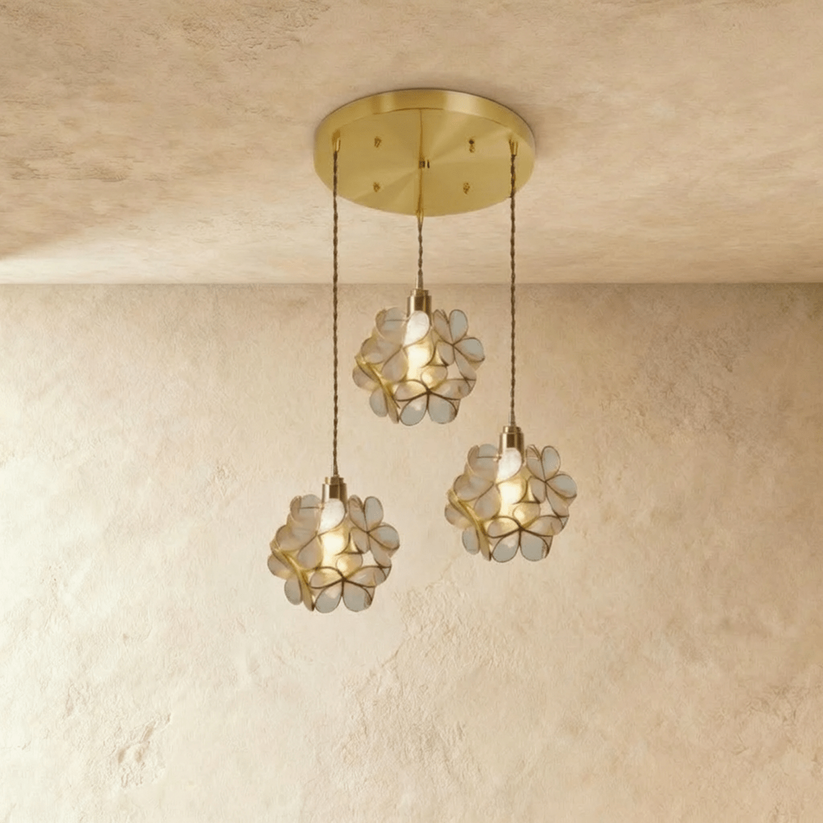 Clérachic three clear glass petal pendants hung at staggered heights from a round brass ceiling plate, on limewash.