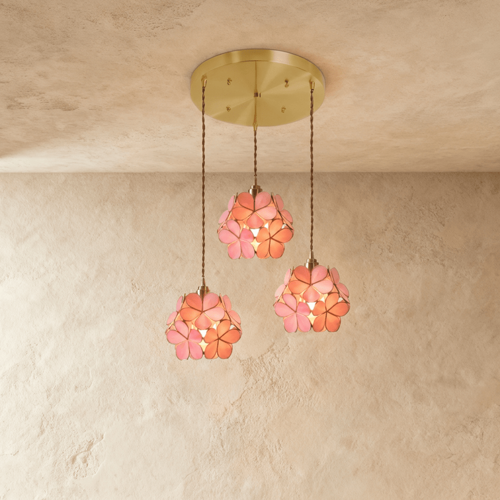 Clérachic three pink glass petal pendants at staggered heights from a round brass ceiling plate, against limewash.