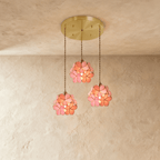 Clérachic three pink glass petal pendants at staggered heights from a round brass ceiling plate, against limewash.