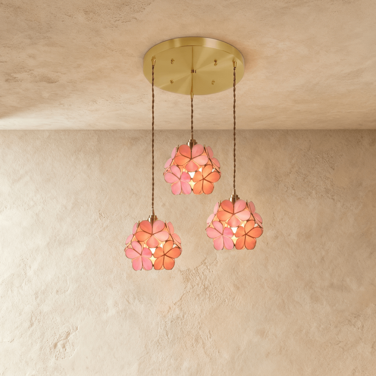 Clérachic three pink glass petal pendants at staggered heights from a round brass ceiling plate, against limewash.