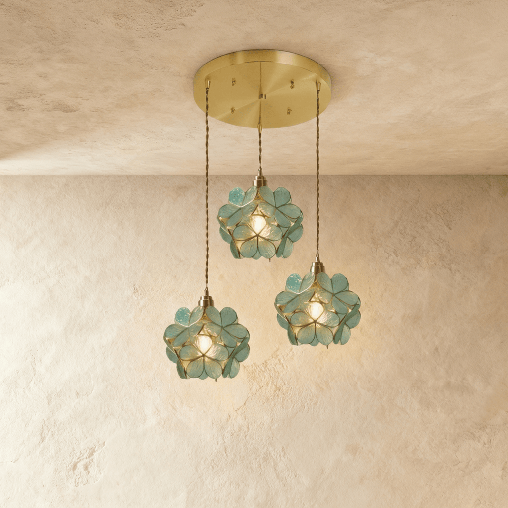 Clérachic three blue-green glass petal pendants at staggered heights from a round brass ceiling plate, on limewash.