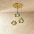 Clérachic three blue-green glass petal pendants at staggered heights from a round brass ceiling plate, on limewash.