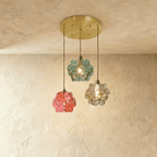Clérachic three petal pendants in blue-green, coral pink and clear glass from a round brass plate, against limewash.