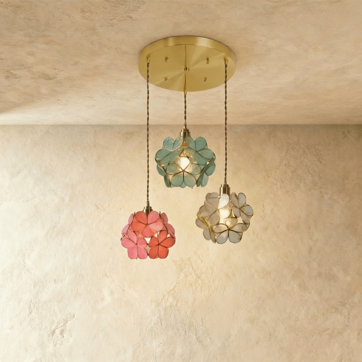 Clérachic three petal pendants in blue-green, coral pink and clear glass from a round brass plate, against limewash.
