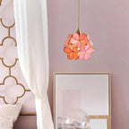 Clérachic pink and coral glass petal pendant beside a bed with a white canopy curtain, against a dusty rose wall.