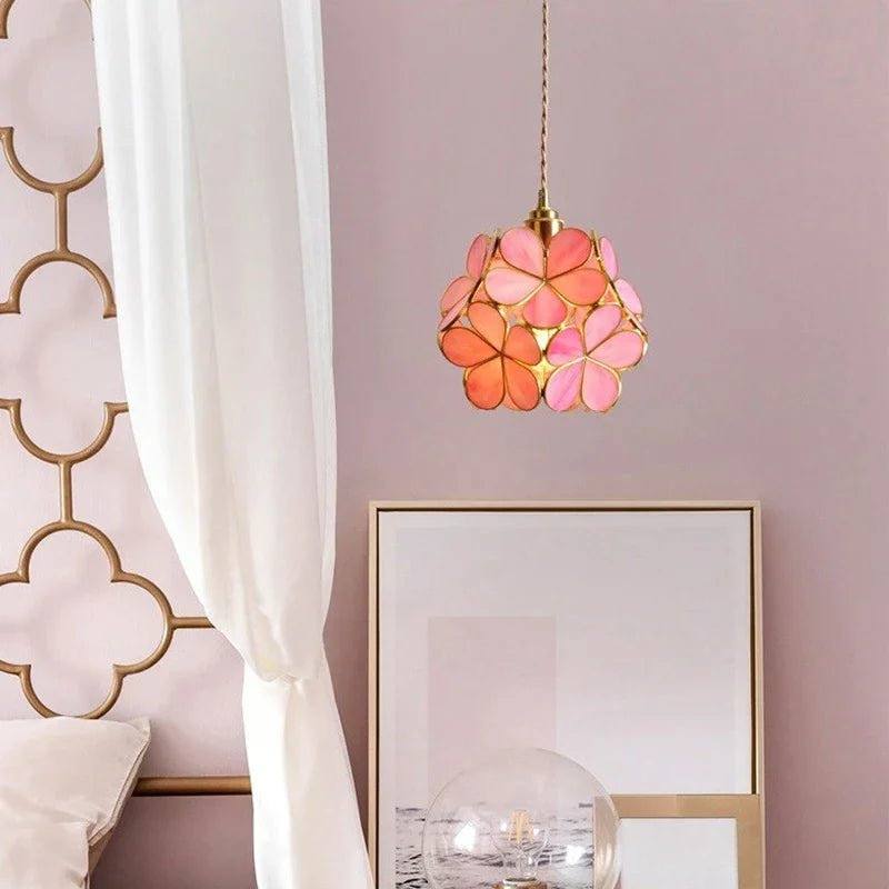 Clérachic pink and coral glass petal pendant beside a bed with a white canopy curtain, against a dusty rose wall.