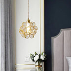 Clérachic clear glass petal pendant edged in brass beside a navy panel and a grey headboard, above white roses in a vase.