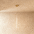 Clérachic slim gold pendant with a glowing opal rod between brass end caps, hung from a round ceiling plate on a fine wire.