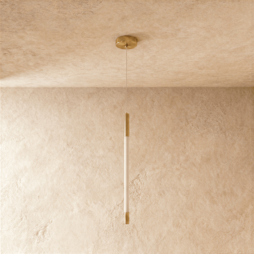 Clérachic gold pendant with an unlit opal rod between brass end caps, hanging from a round gold ceiling canopy on thin wire.