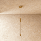 Clérachic gold pendant with an unlit opal rod between brass end caps, hanging from a round gold ceiling canopy on thin wire.