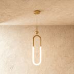 Clérachic gold pendant with a tall U-shaped brass frame, a glowing opal lower tube and a small ball above, hung on wire.