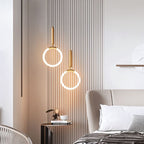 Clérachic pair of gold ring pendants glowing at different heights before a slatted wall beside a bed and side table.