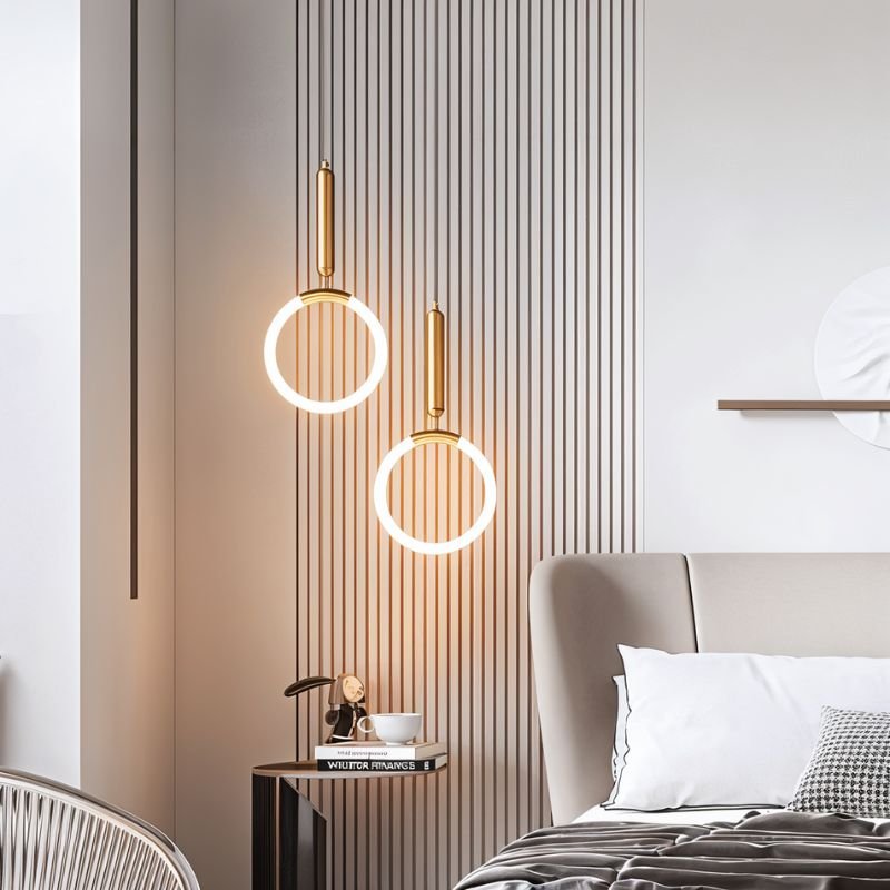 Clérachic pair of gold ring pendants glowing at different heights before a slatted wall beside a bed and side table.