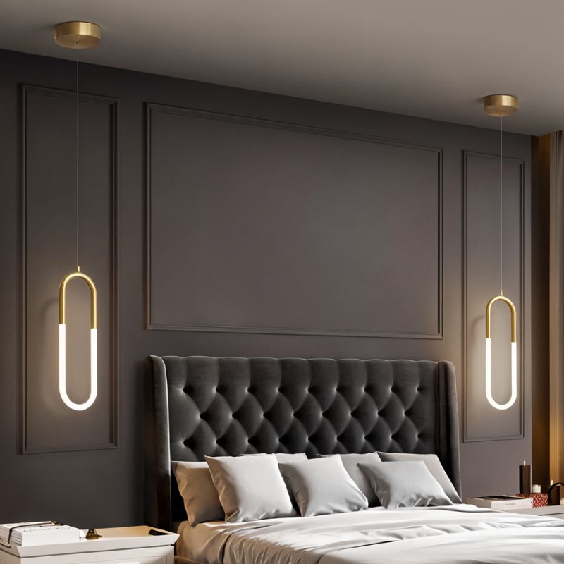 Clérachic two gold U-shaped pendants with glowing opal tubes hung either side of a tufted grey headboard on a dark wall.