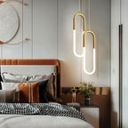 Clérachic pair of gold U-shaped pendants with glowing opal tubes hung at staggered heights above a bedside table.