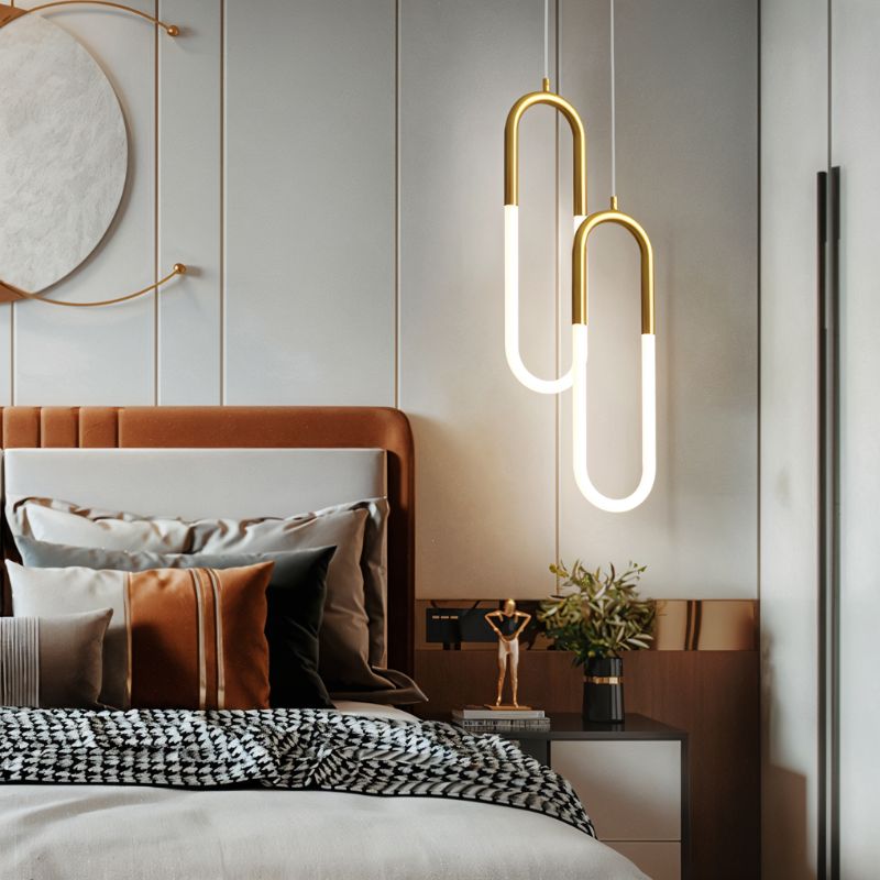Clérachic pair of gold U-shaped pendants with glowing opal tubes hung at staggered heights above a bedside table.