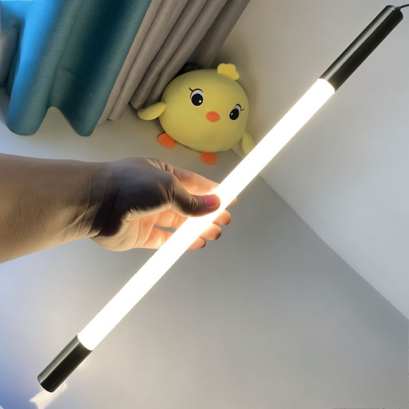 Clérachic opal LED tube with dark end caps, held in one hand and lit warm white, shown beside a soft toy and curtain.