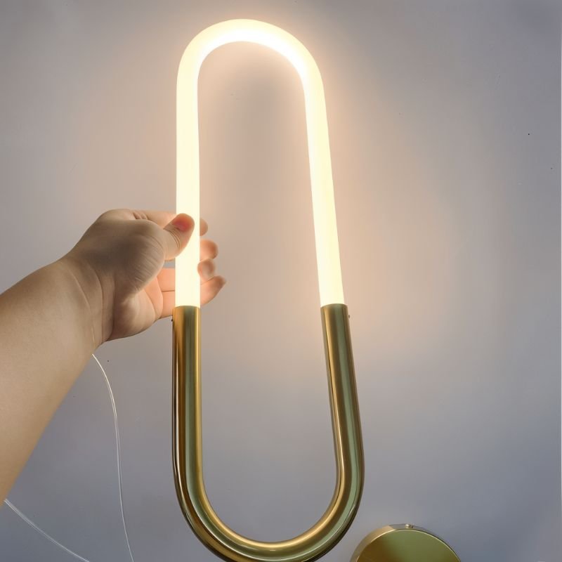 Clérachic hand holding a lit opal U-shaped tube above a brass base, with a gold round plate at the lower edge.