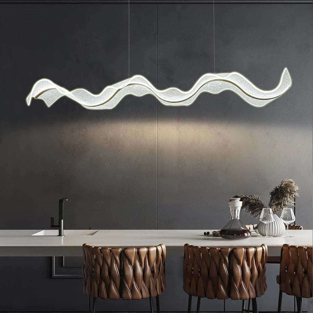 Lit Clérachic pendant with a rippling wave shape above a pale kitchen island, with brown quilted bar stools below against a dark grey wall.
