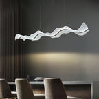 Side view of this Clérachic pendant over dark upholstered dining chairs, a warm pool of light falling on the grey wall behind.