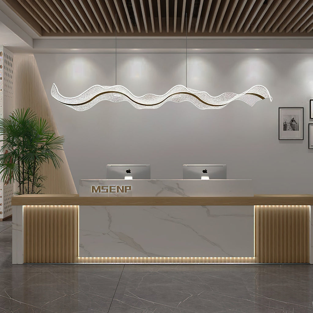 Wave-shaped Clérachic pendant hanging in a wide reception area, above a white marble counter with gold-toned slatted panels.