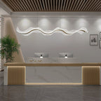 Wave-shaped Clérachic pendant hanging in a wide reception area, above a white marble counter with gold-toned slatted panels.