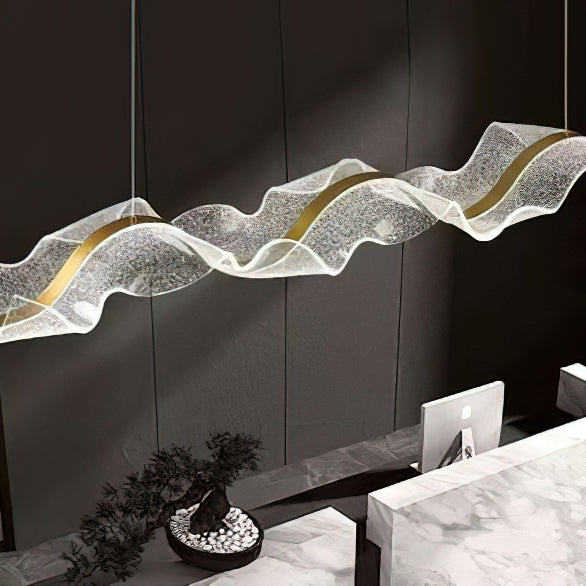 Near view of the speckled acrylic wave and curving gold strip on this Clérachic pendant, over a marble desk with a small potted tree.