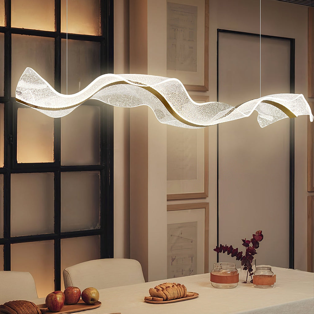 Brightly lit Clérachic pendant with a glowing acrylic wave above a white dining table set with fruit, bread and small candles.