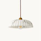 Scalloped white shade with grey veining on a twisted brown cord and a gold cap, a Clérachic pendant with a bulb showing, on a plain backdrop.