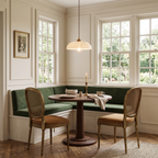 A small Clérachic pendant with a ribbed white shade hangs over a round wooden table in a window nook with a green bench seat.