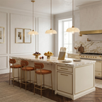 Three Clérachic pendants with ribbed white shades hang in a line over a cream kitchen island with a marble top and tan stools.