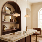 Two Clérachic ribbed shade pendants glow in a cream room with an arched wooden shelf, a marble counter and a brown leather stool.