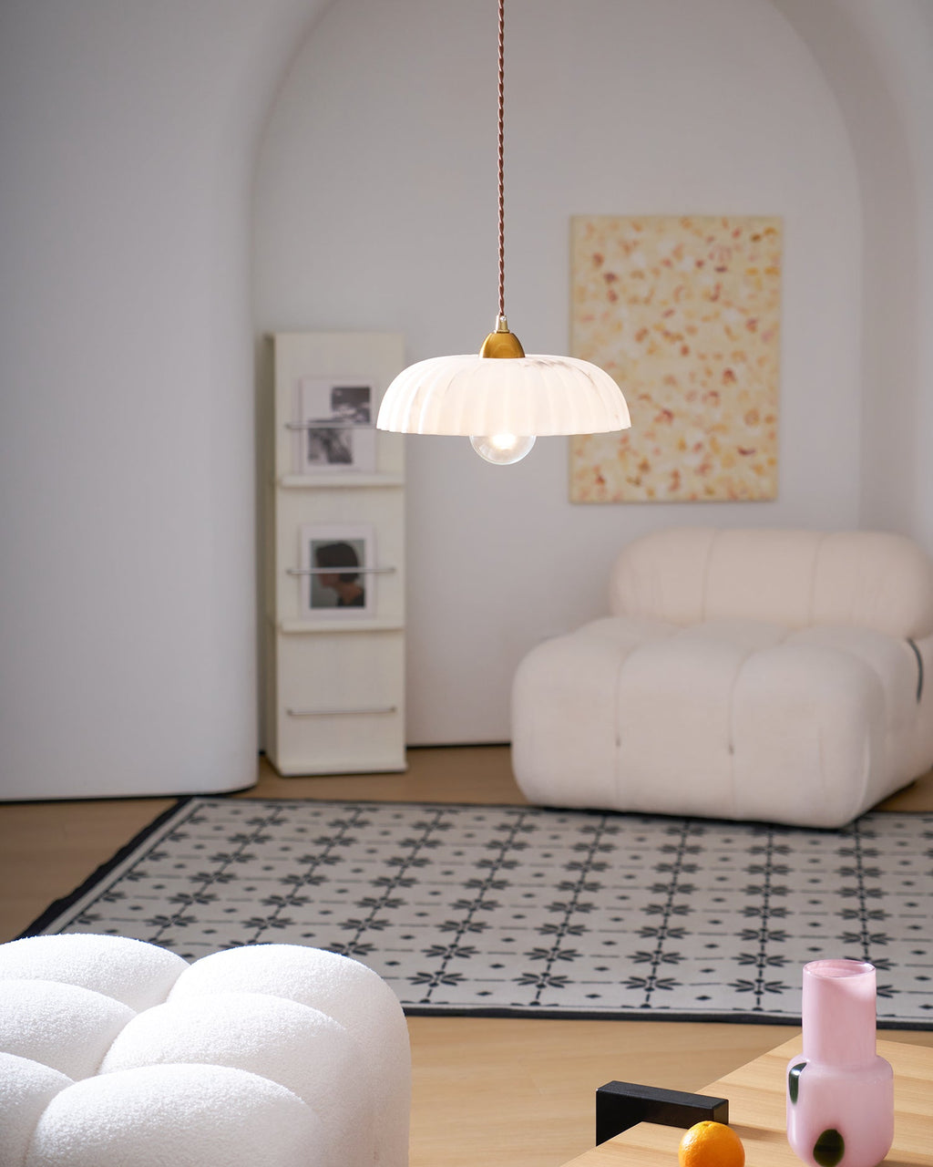 Ribbed white Clérachic pendant glows in a pale arched room with a cream bouclé chair and a patterned tile rug.