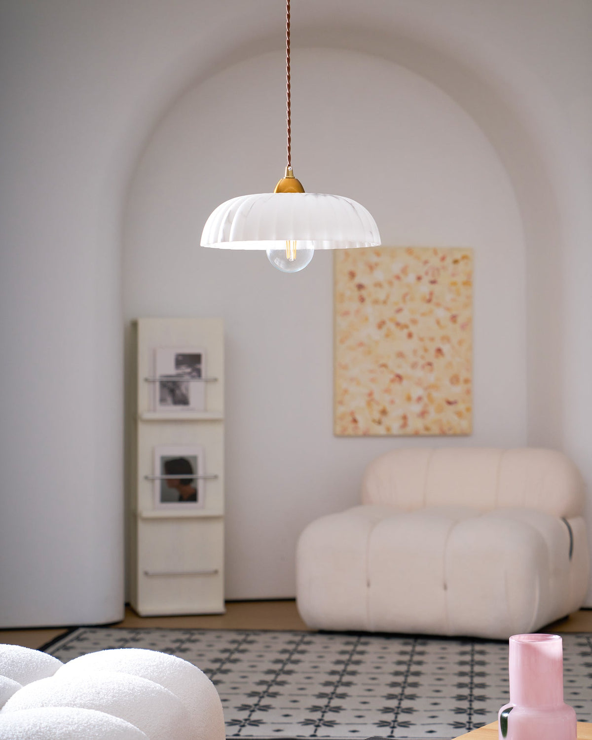 A Clérachic ribbed white pendant in an arched room, seen from further back, with a cream chair and a patterned tile rug.