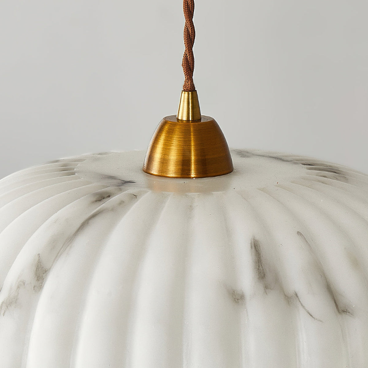 Close view of the gold cap and gathered ribs at the top of this Clérachic pendant's marbled white shade.