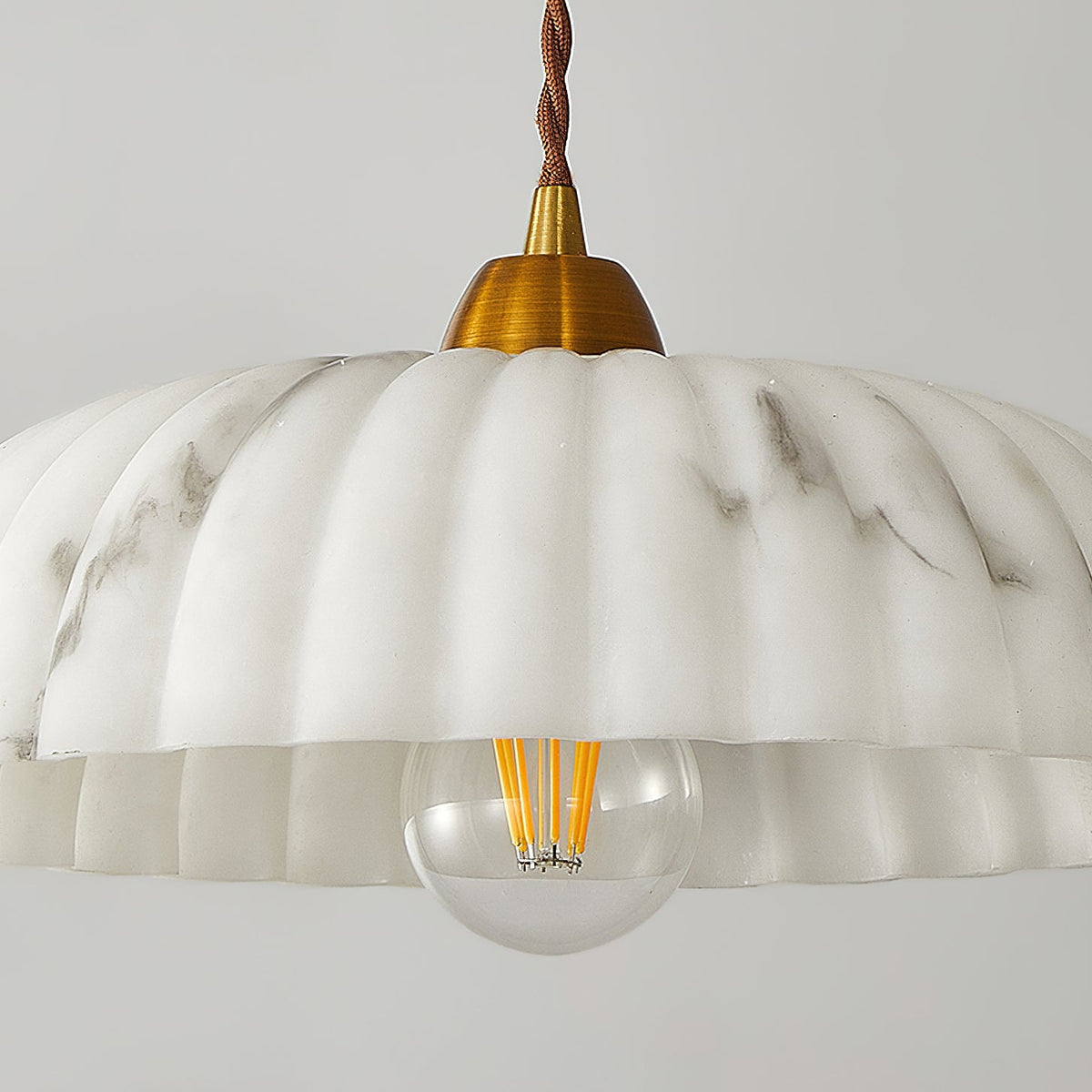 Close view of the scalloped rim and filament bulb of this Clérachic pendant, with soft grey veining running through the shade.