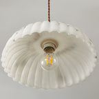 View from below into the white scalloped shade of this Clérachic pendant, with its ceramic socket and filament bulb in the centre.