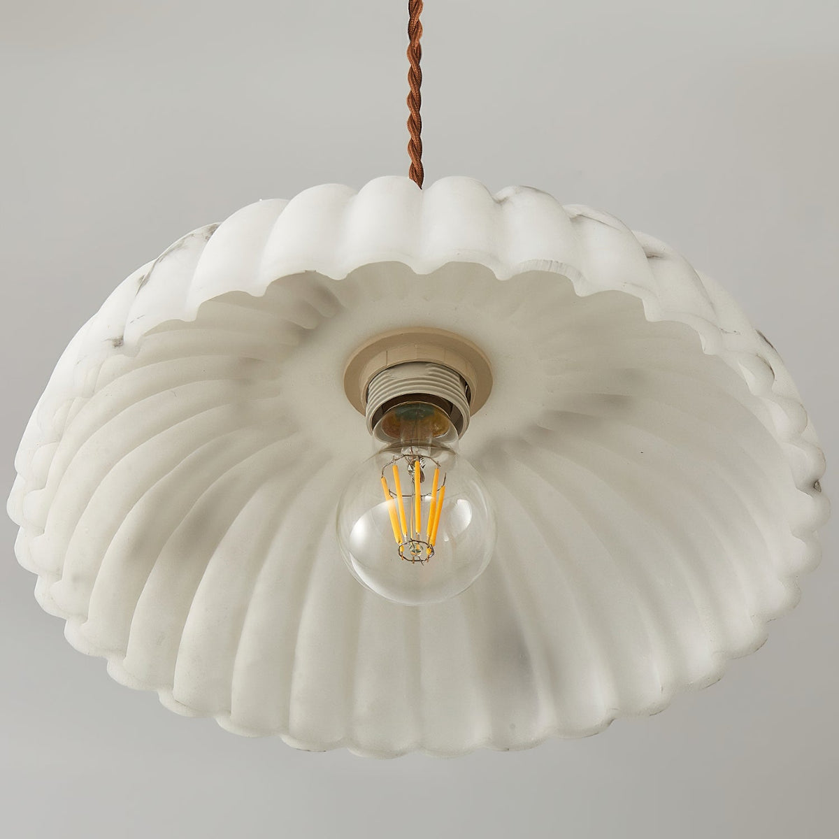 View from below into the white scalloped shade of this Clérachic pendant, with its ceramic socket and filament bulb in the centre.